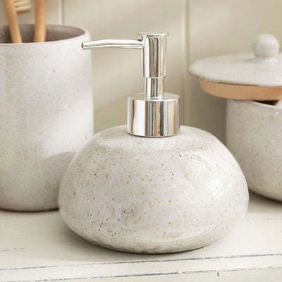Stone effect ceramic lotion dispenser with toothbrush holder and lidded jar on a bathroom counter.