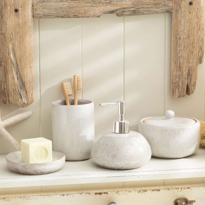 Stone effect ceramic bathroom accessory set with soap dish, toothbrush holder, lotion dispenser, and lidded jar on a wooden shelf.
